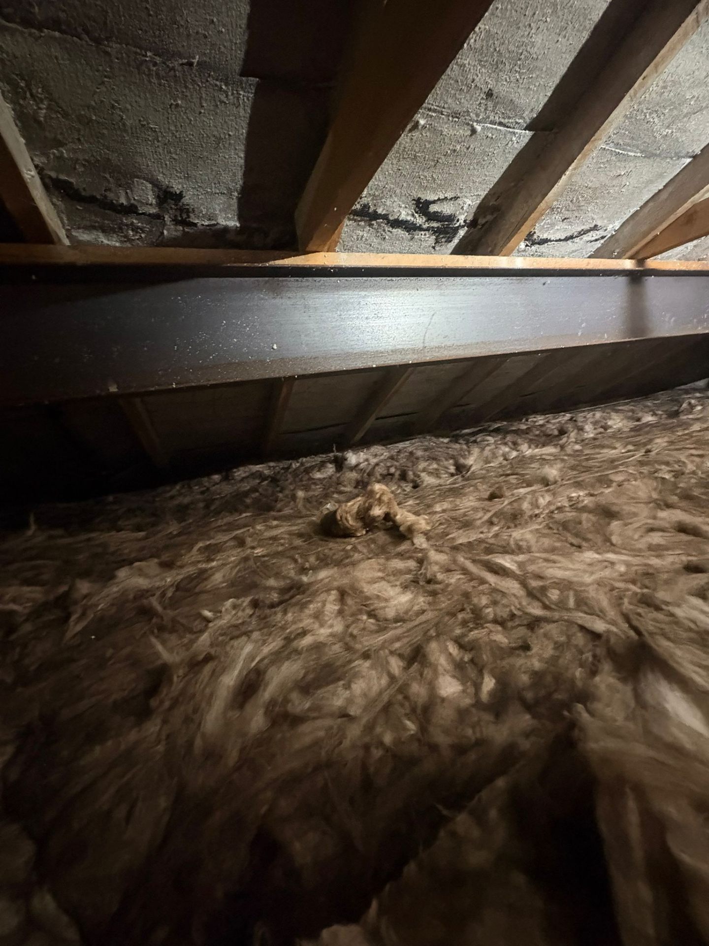 Aged spray foam on roof underside above old mineral wool needing removal